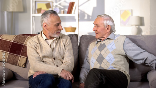 Positive senior men looking each other sitting home sofa, friendship emotions