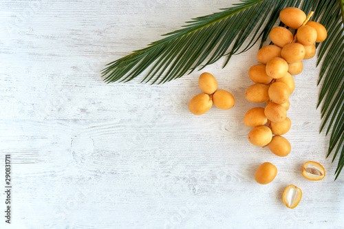 Fresh raw yellow dates with palm leaf on white wooden background. Top view	