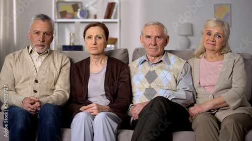 Upset senior friends sitting sofa looking camera, social problems, retirement