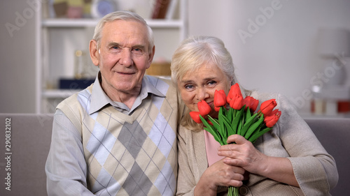 Smiling mature husband and wife with tulips looking camera, holiday celebration © motortion