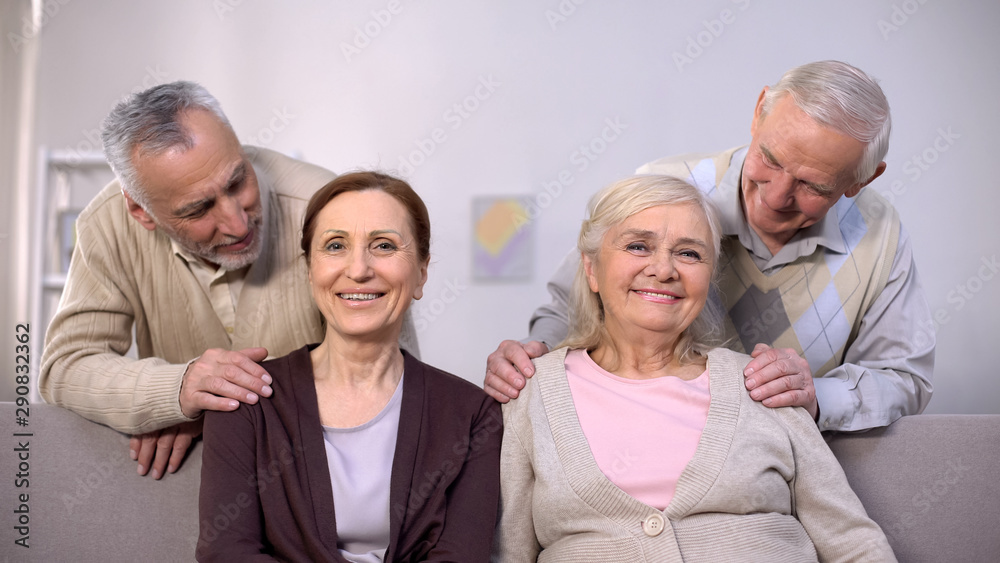 Happy aged men looking mature smiling wives sitting sofa, retirement happiness Happy aged men looking mature smiling wives sitting sofa, retirement happiness