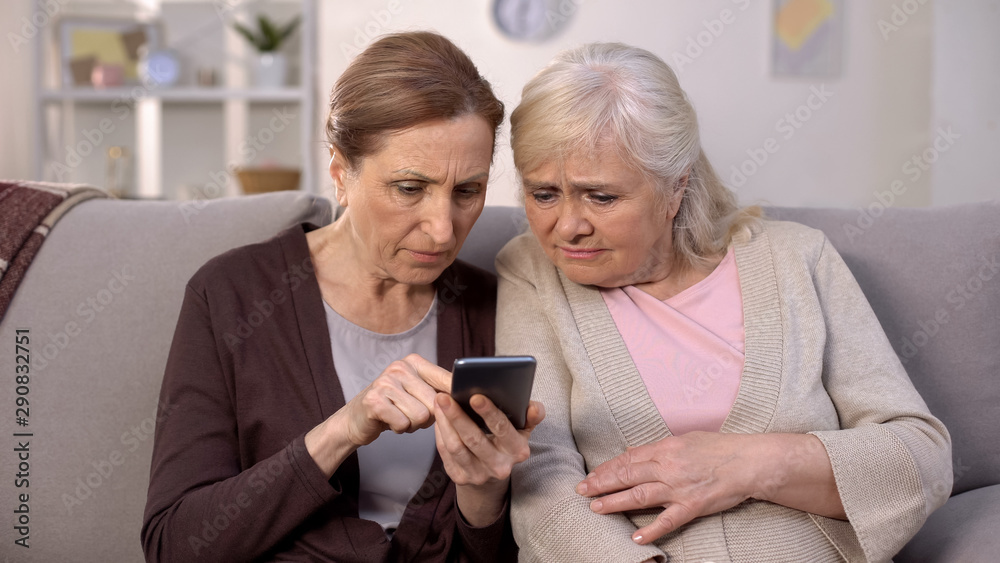 Two mature ladies learning use smartphone sitting home sofa, old age technology Two mature ladies learning use smartphone sitting home sofa, old age technology