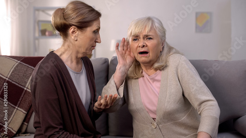 Tablou pe pânză Old deaf woman listening senior friend, hearing disease, old age health care