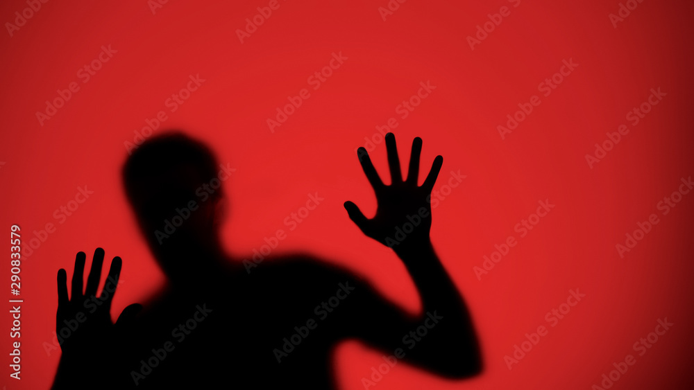 Injured male silhouette behind glass, red lights background, warfare concept