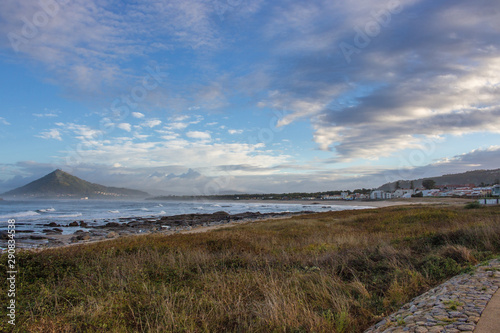 Mountain on ocean coast in the morning. Scenic landscape near Caminha, Portugal. Panoramic seascape with stones in water and green hill on horizon. Camino de Santiago landscape.  photo