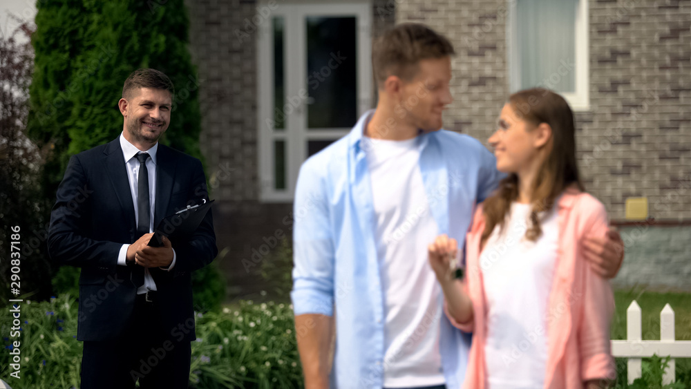 Estate broker watching happy couple enjoying new house showing keys to camera Estate broker watching happy couple enjoying new house showing keys to camera