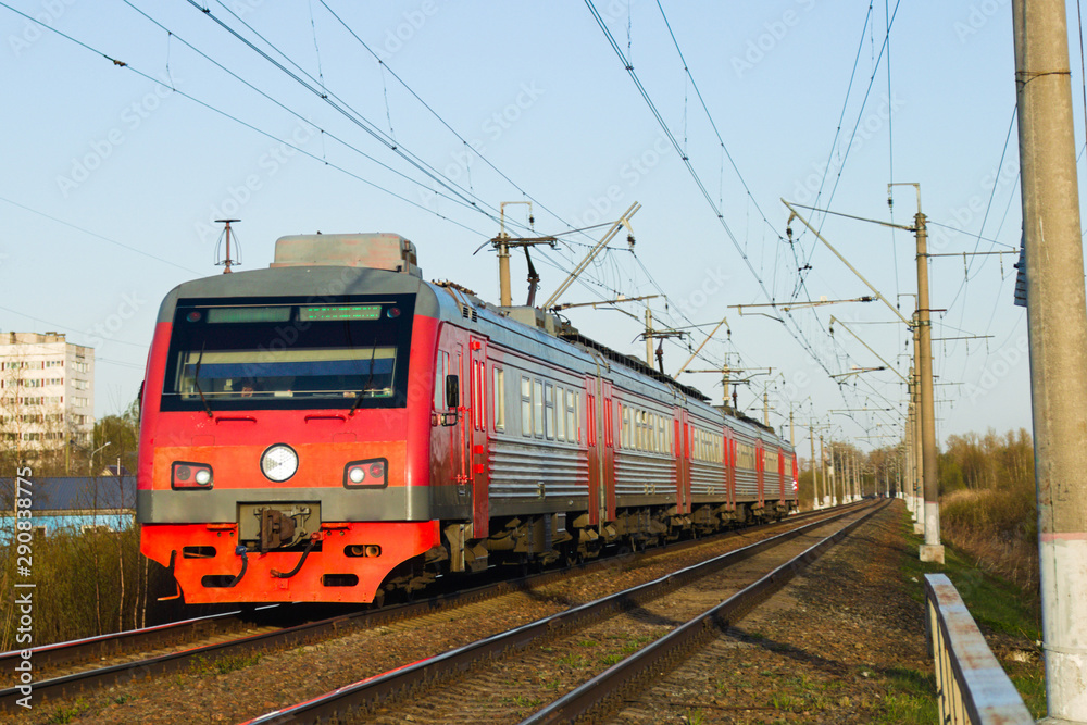 The red electric train travels along the railway lines towards the summer. Suburban passenger rail service.