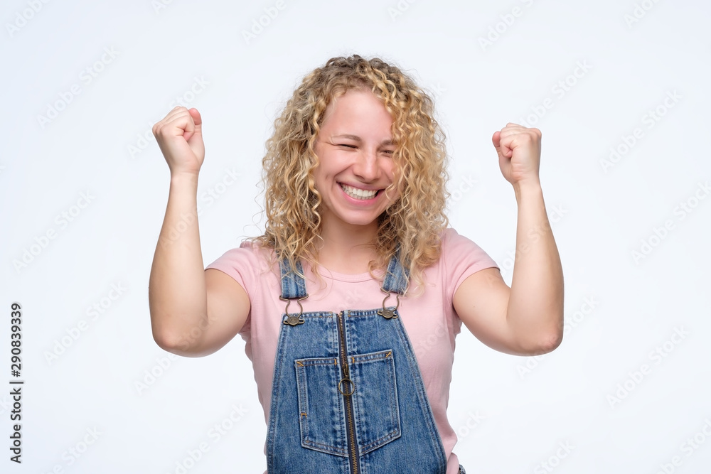 Happy elegant blonde curly girl celebrating her success and looking at camera. Positive facial human emotion