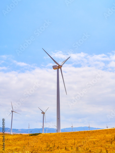 Wind turbines between an arid field and a blue sky background for copy space.