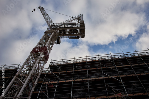 The underside of a tall construction crane rising above scaffolding on a cloudy day.