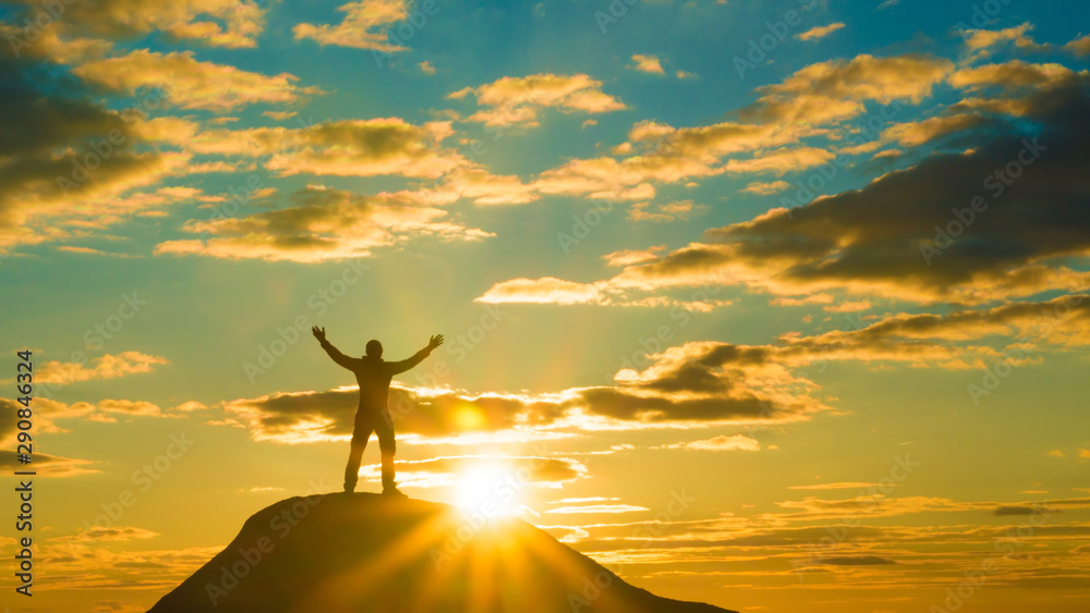 Happy man on top of a mountain holding his hands up. against the sunset. Success and achievement, winner.