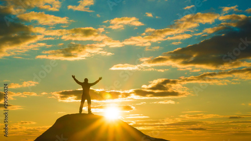 Happy man on top of a mountain holding his hands up. against the sunset. Success and achievement, winner.