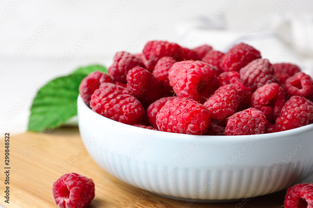 Bowl with delicious ripe raspberries on wooden cutting board, closeup Bowl with delicious ripe raspberries on wooden cutting board, closeup