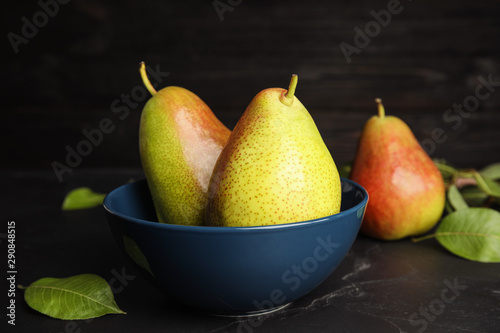 Bowl with ripe juicy pears on black stone table against dark background