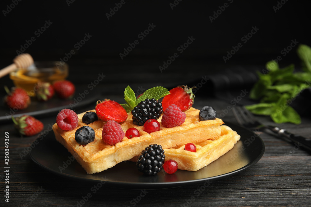 Delicious waffles with fresh berries served on black wooden table Delicious waffles with fresh berries served on black wooden table