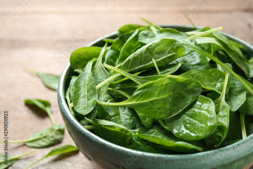 Bowl of fresh green healthy spinach on wooden table, closeup