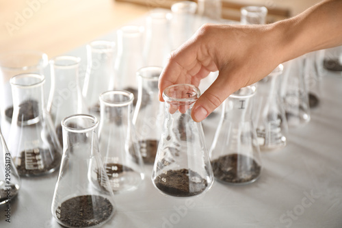 Woman holding flask with soil sample over table, closeup. Laboratory analysis