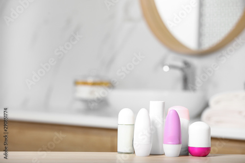 Different female deodorants on wooden table in bathroom, space for text