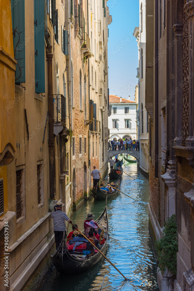 Narrow canal in Venice, Italy, with gondolas and historic houses, in a beautiful sunny day.