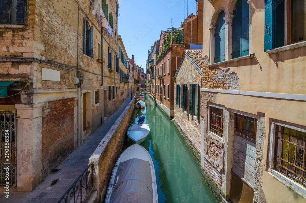 Narrow canal in Venice, Italy, with boats and historic houses, in a beautiful sunny day.