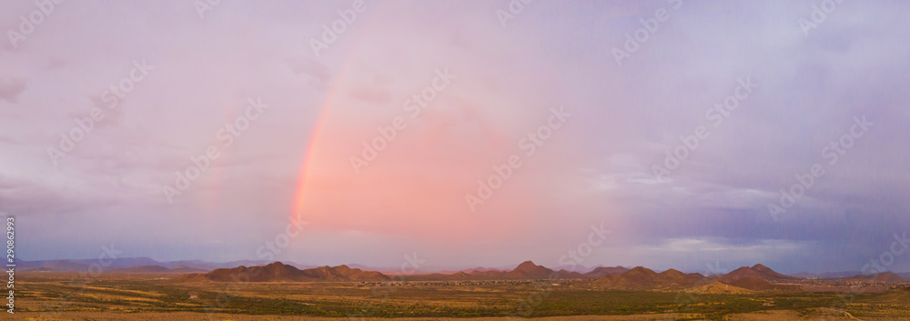 A panorama of an Arizona monsoon with a rainbow and mountains in the distance.
