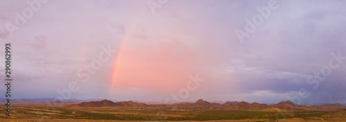 A panorama of an Arizona monsoon with a rainbow and mountains in the distance.