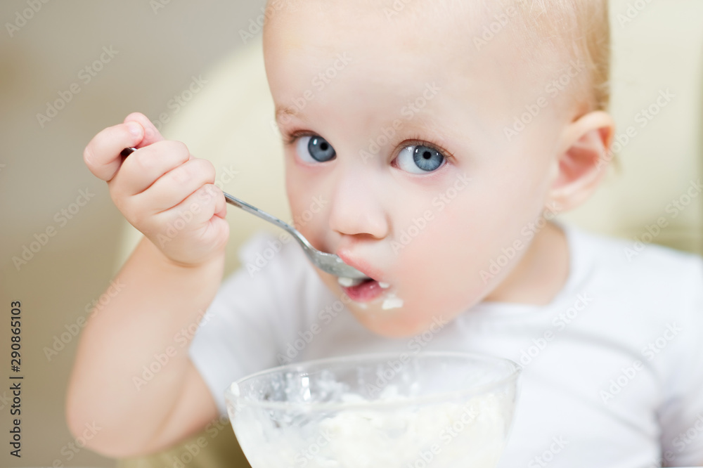 little girl with blue eyes eating porridge with a metal spoon. Close up little girl with blue eyes eating porridge with a metal spoon. Close up
