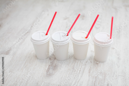 four white paper cups with red tubes for coffee to go on white wooden table in selective focus.