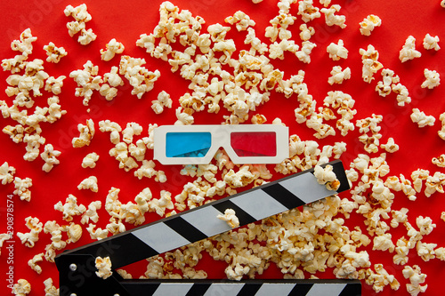 top view of delicious popcorn scattered on red background near clapper board and 3d glasses