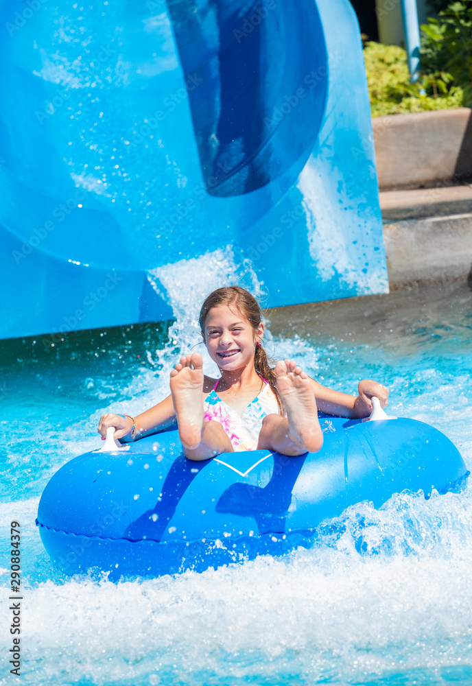 Smiling Cute little girl riding down a water slide at a water park with ...