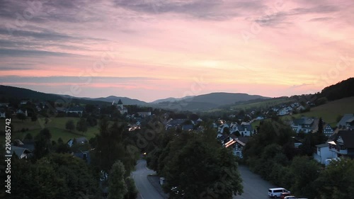 Wide panoramic pan over the mountainous spa village of Grafschaft in the winter sports region of Sauerland, Germany, during sunset with a colourful purple and orange lit cloudy sky photo