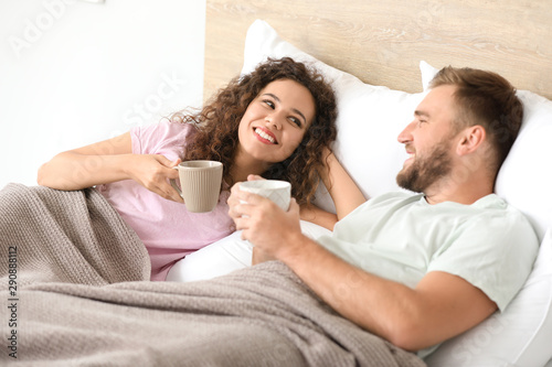 Happy young couple drinking coffee while relaxing in bed