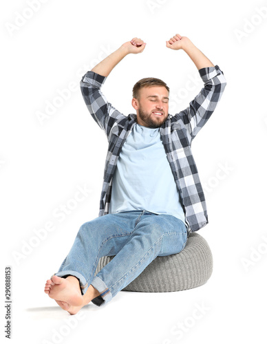 Handsome young man relaxing on pouf against white background
