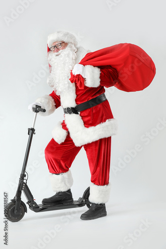 Santa Claus with scooter and gifts on white background