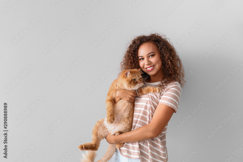 Young African-American woman with cute cat on light background