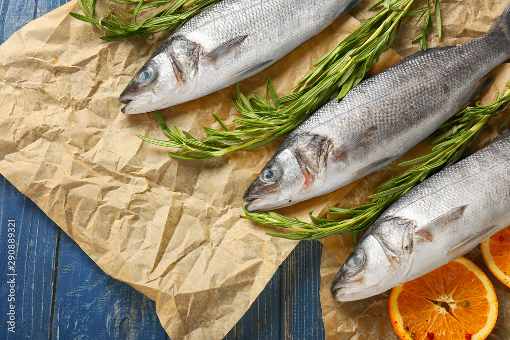 Fresh seabass fish with orange and rosemary on wooden background