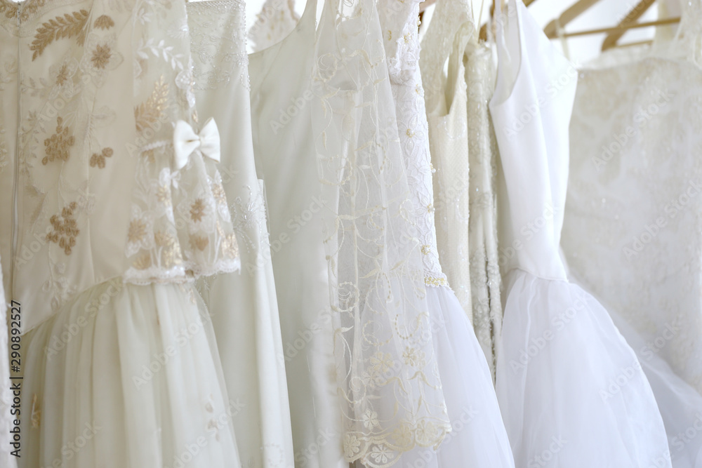 Wedding white gown for bride hanged in costume showroom for marriage or wedding reception. White delicated lace on long dress for promp or party Wedding white gown for bride hanged in costume showroom for marriage or wedding reception. White delicated lace on long dress for promp or party