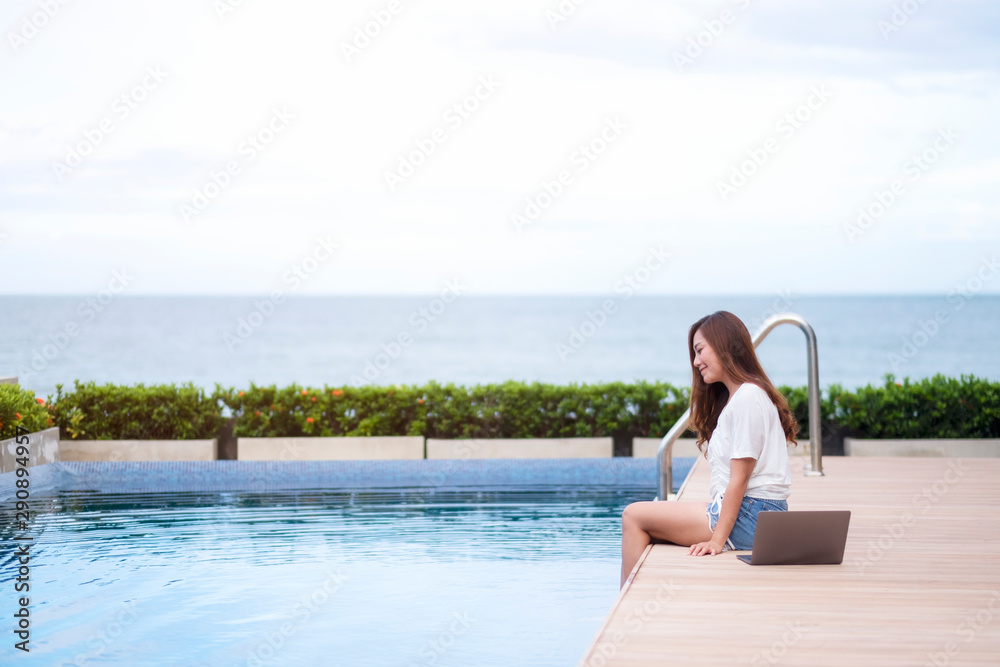 A beautiful asian woman sitting by swimming pool with laptop computer