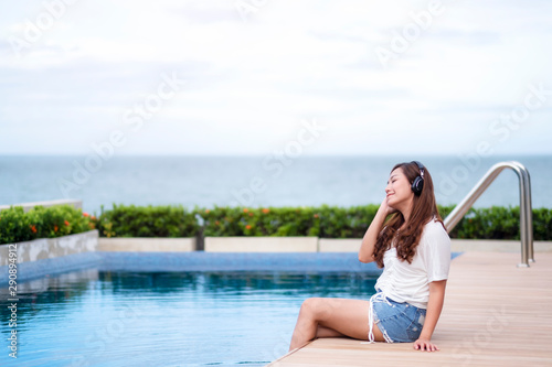 A beautiful asian woman listening to music  with headphone while sitting by swimming pool © Farknot Architect