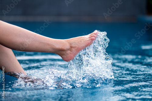 Closeup image of legs and right foot kicking and splashing water in the pool