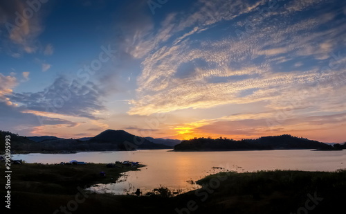 Lake view evening of many camping tents on the bank around with the hills and yellow sun light with cloudy sky background, sunset at Kaengkrachan National Park, Phetchaburi, Thailand. © Yuttana Joe