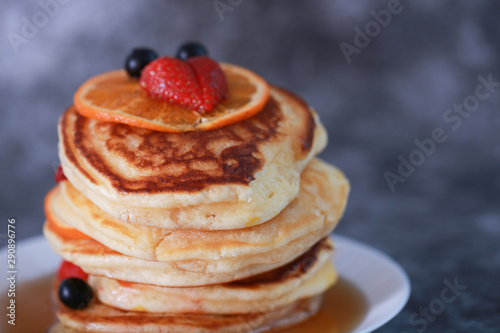 Pancake with orange, strawberry and blueberry on top with maple syrup. Sweet honey pour on pancake layer with grunge background