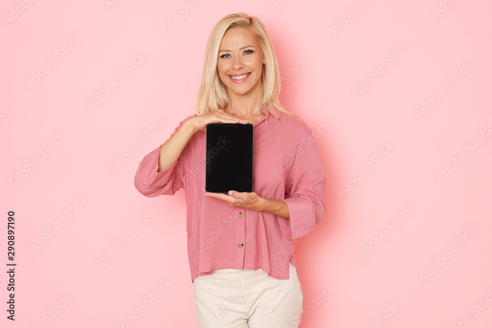 Beautiful woman in pink background is presenting a digital tablet.