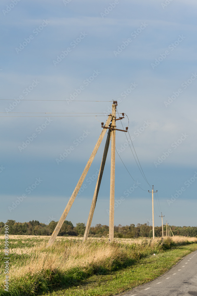 Fototapeta premium Old fashioned electricity post and on the golden yellow crop field in early autumn. Calm blue skyline, green row of forest in the background. Countryside in tiny North European country Estonia.