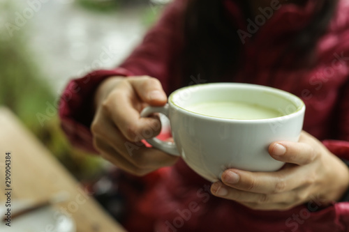 Green tea, hot matcha latte in white ceramic cup with saucer on young woman hand with cinnamon