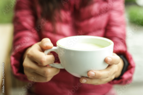 Green tea   hot matcha latte in white ceramic cup with saucer on young woman hand with cinnamon