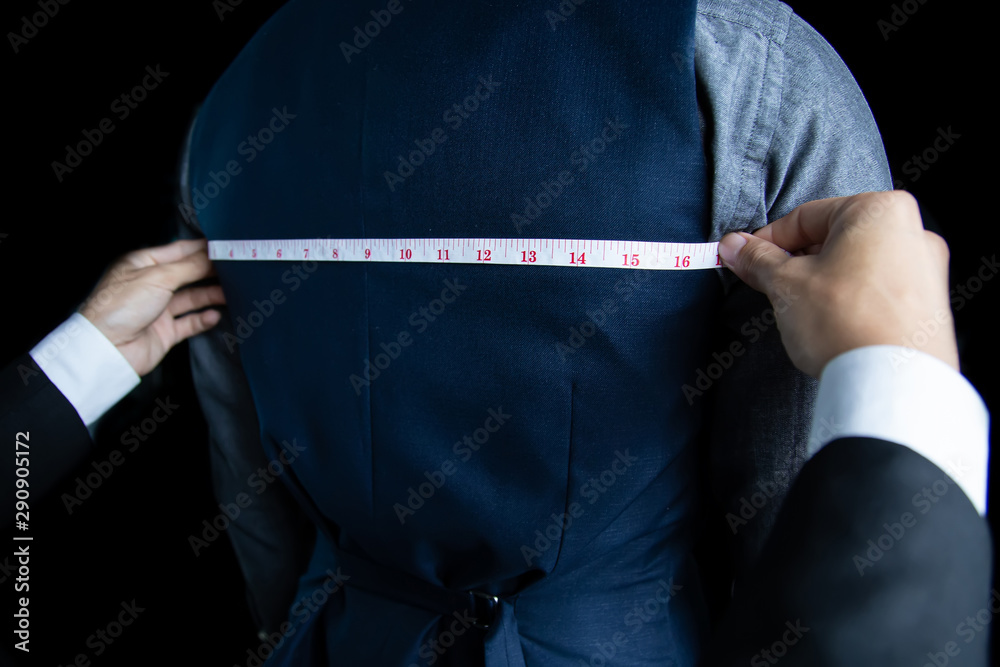 Φωτογραφία The dressmaker was measuring the width of the back of the man wearing a blue suit on black background