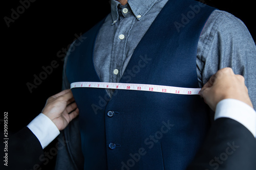 The dressmaker was measuring the chest width of a man wearing a blue suit.