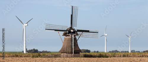 old windmill and modern turbines together in agricultutre landscape of friesland