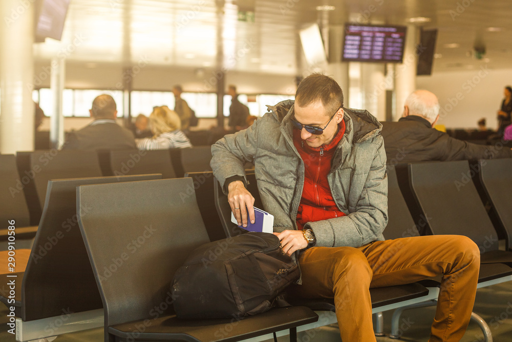 Mature businessman using mobile phone at the airport in the waiting room. Business man typing on smartphone in lounge area. Portrait of latin man sitting and holding passport with luggage.